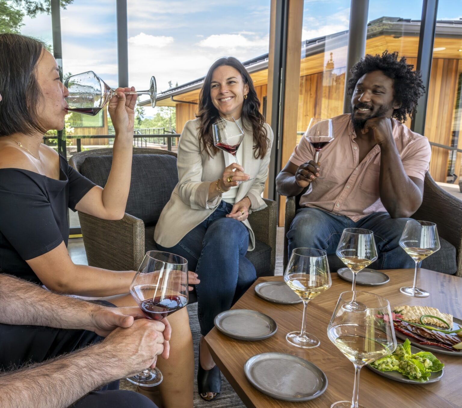 A group of four people are seated at a table, enjoying glasses of Willamette Valley Chardonnay and engaging in conversation. Various wine glasses and plates are on the table, creating a warm and convivial atmosphere.